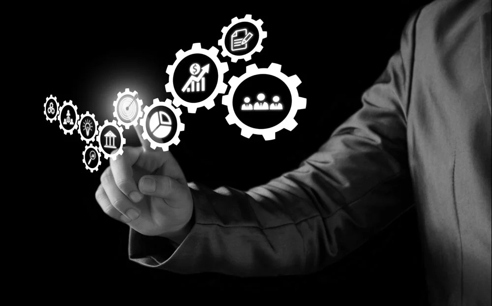 Hand eines Geschäftsmanns, die auf virtuelle Geschäftssymbole auf einem Bildschirm zeigt.